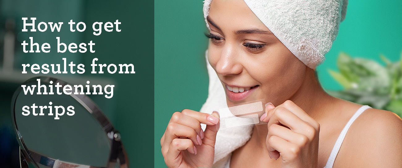 A woman with a towel wrapped around her head smiles while holding a pair of teeth whitening strips. She is looking at a mirror, preparing to apply them. The text on the left side reads, "How to get the best results from whitening strips.